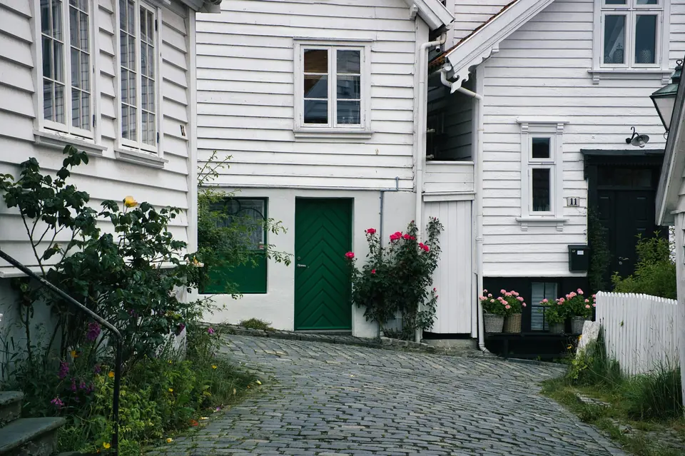 Hvite trehus med grønn dør og roser langs en brosteinsgate